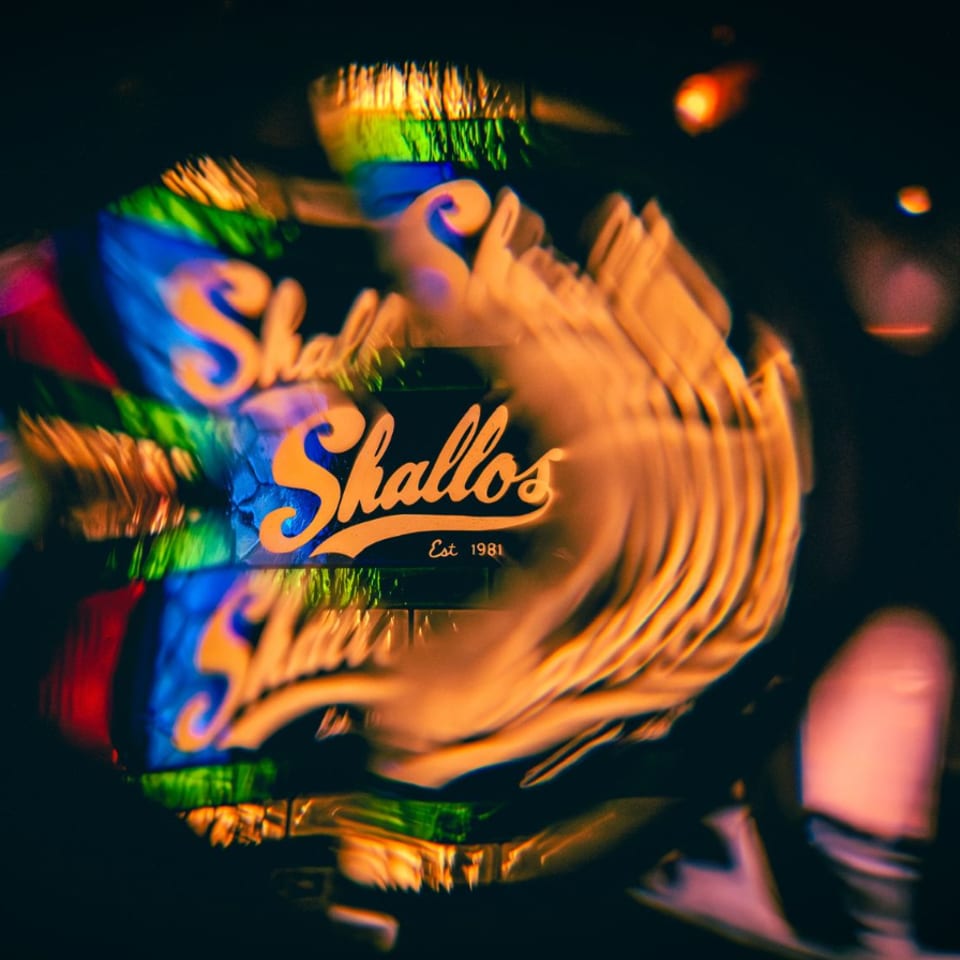 Neon Shallos restaurant sign reflected repeatedly in a dark, colorful window.