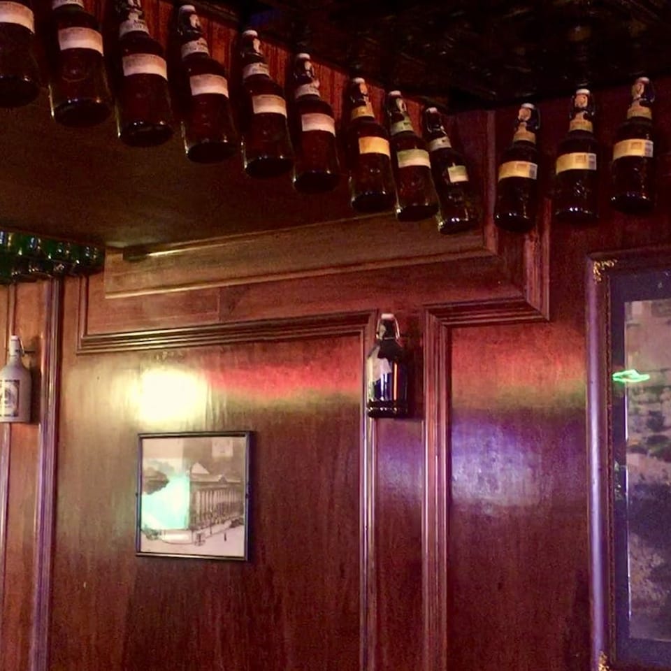 Dark wooden walls adorned with framed pictures and rows of bottles hanging from the ceiling.
