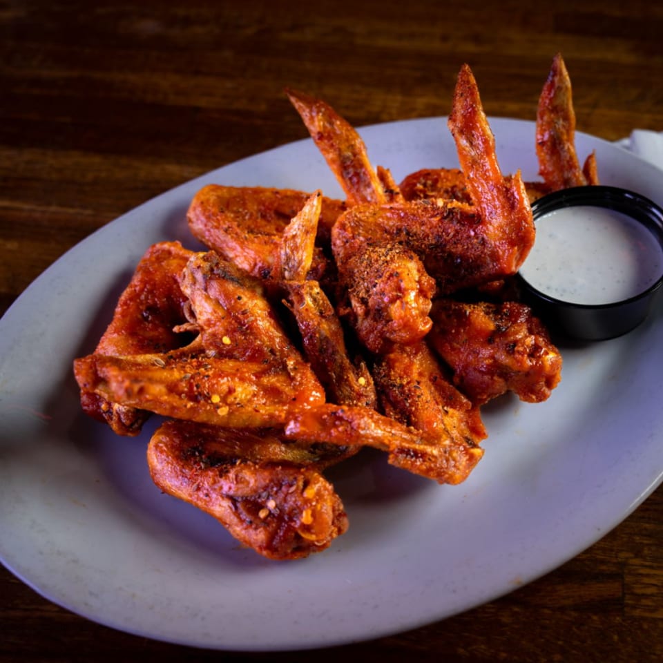 Crispy, spiced chicken wings piled on a gray plate with a side of creamy dipping sauce.