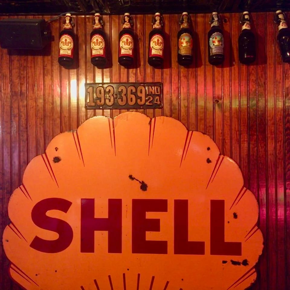 Vintage Shell sign, license plate, and beer bottles decorating a wooden wall.